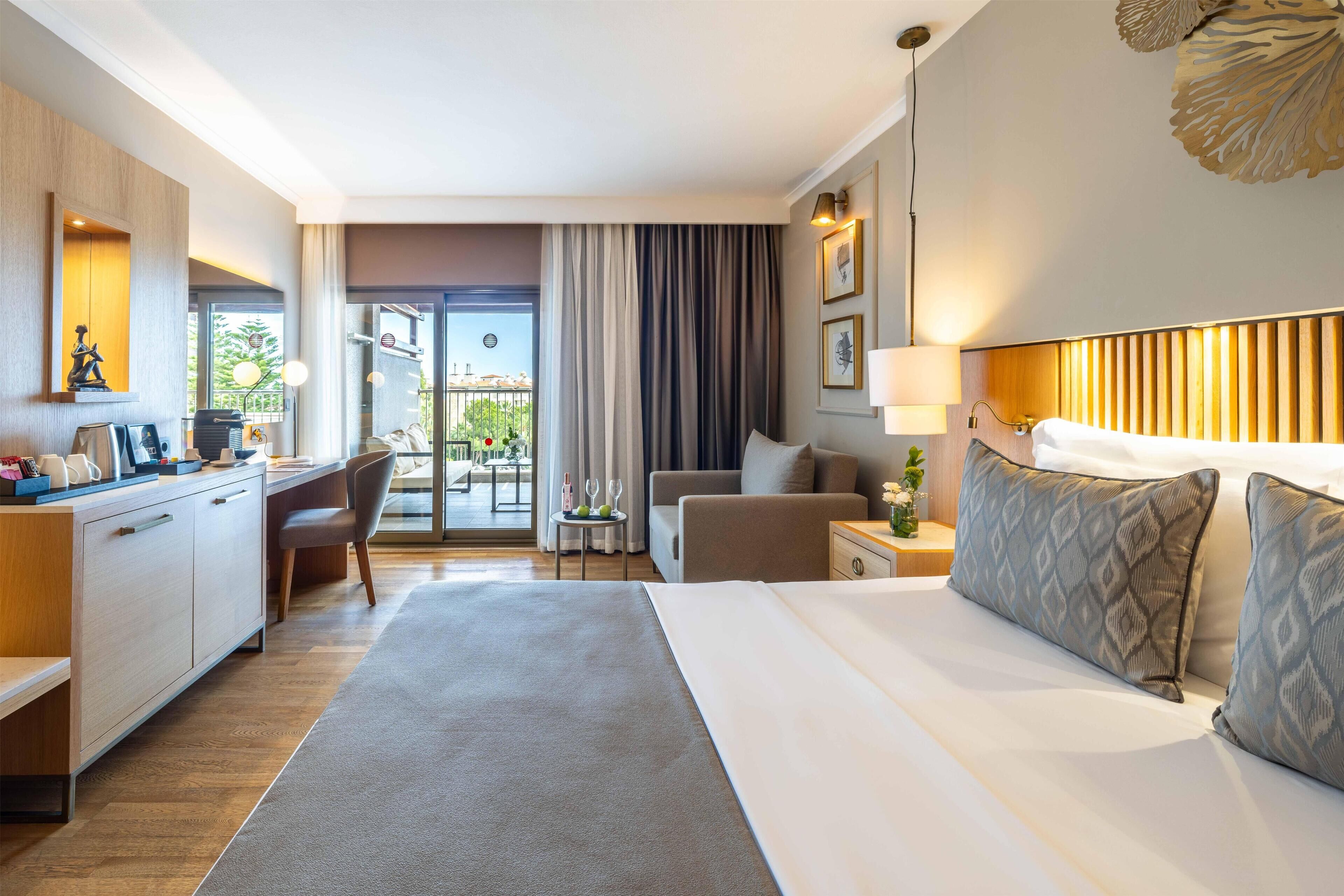 A hotel room with a bed, a desk, a chair, a sofa, and a view of the outdoors.