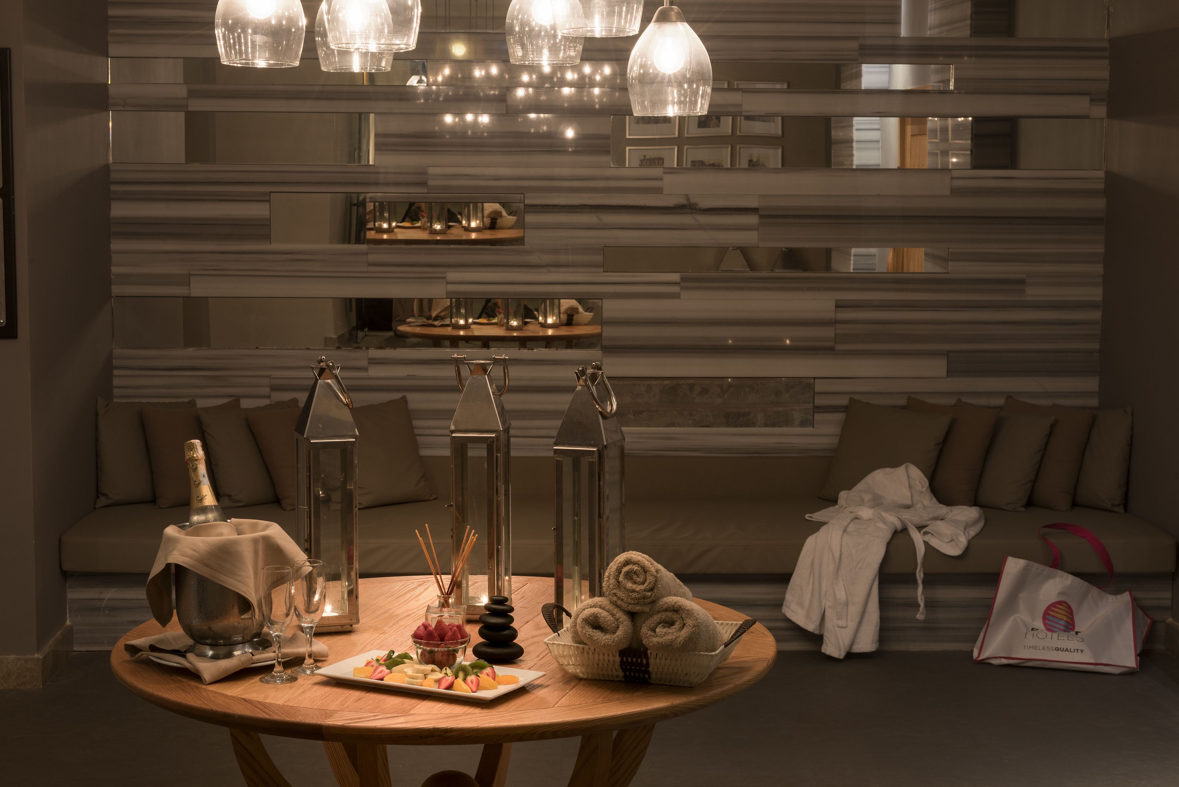 A well-lit room with a round wooden table set for a meal, a bottle of champagne, and a basket of towels.