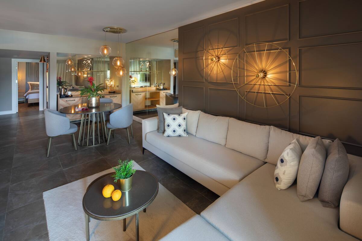 A modern living room with a sofa, a coffee table with fruits, and a dining area with chairs and a table.