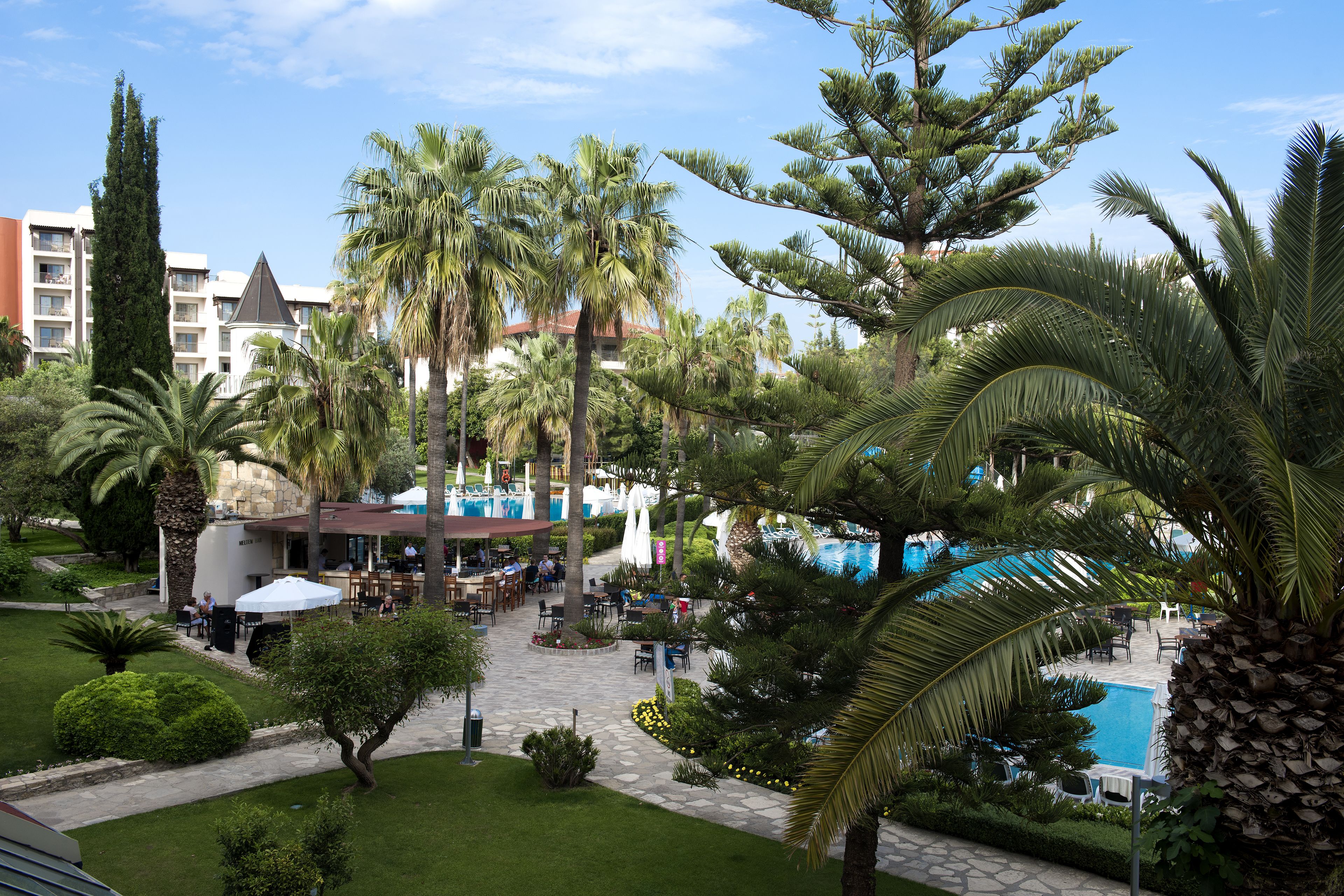 Patio de un resort con mobiliario exterior, piscina y palmeras.
