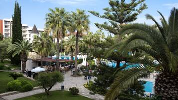 Patio de un resort con mobiliario exterior, piscina y palmeras.