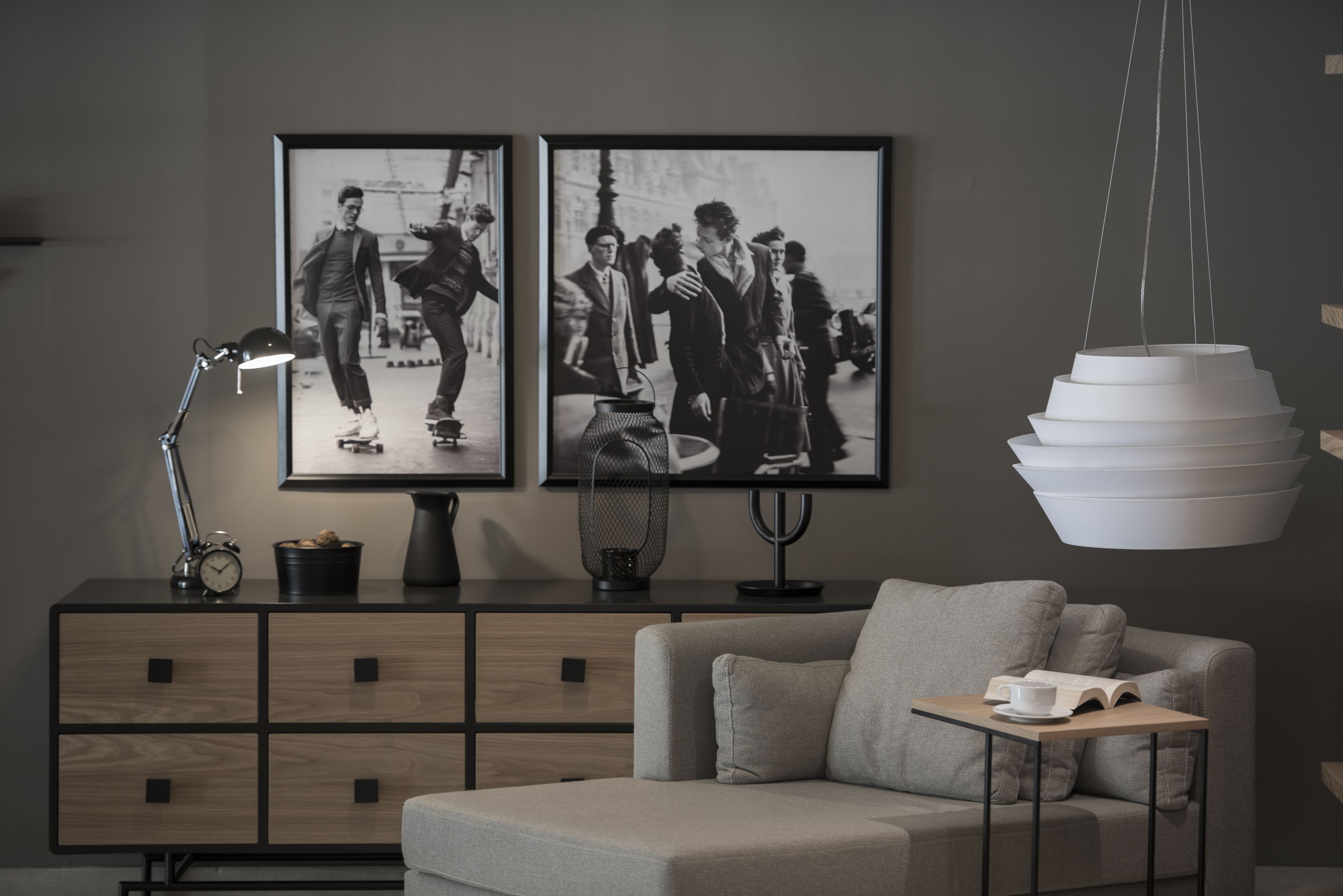 Uma sala de estar moderna com sofá, mesa de centro, mesa lateral, abajur, relógio e duas fotografias a preto e branco emolduradas na parede.
