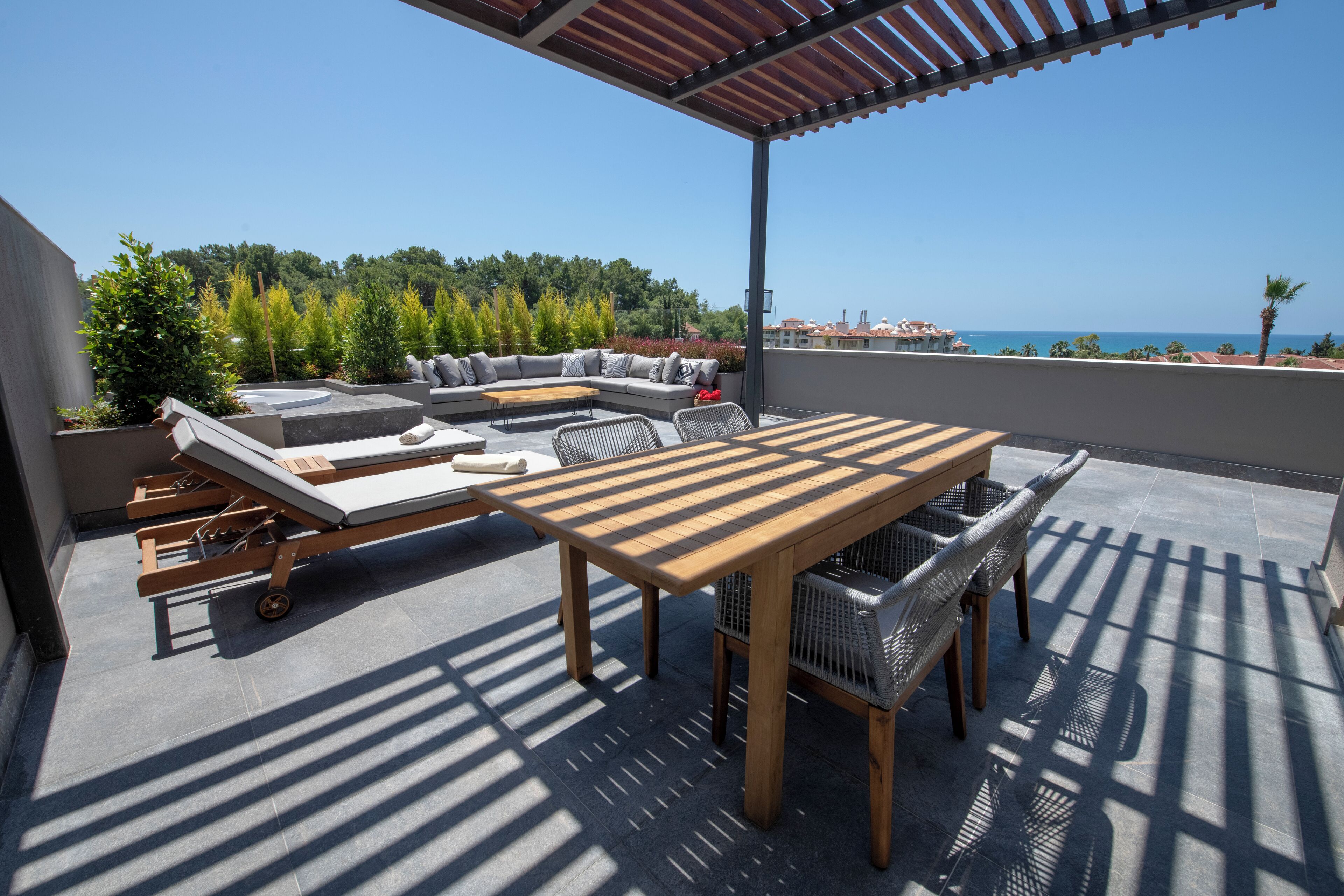 A covered outdoor seating area with a wooden table and chairs, a sofa, and a lounge chair.