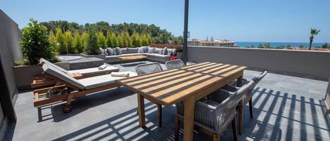 A covered outdoor seating area with a wooden table and chairs, a sofa, and a lounge chair.