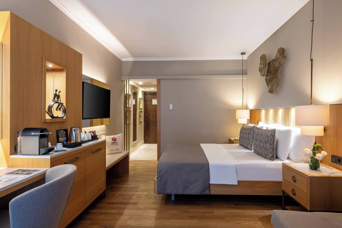 A modern hotel room with a bed, bedside tables, a desk, and a television.