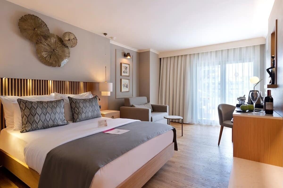 A hotel room with a large bed, a desk, a chair, a lamp, and a window with curtains.