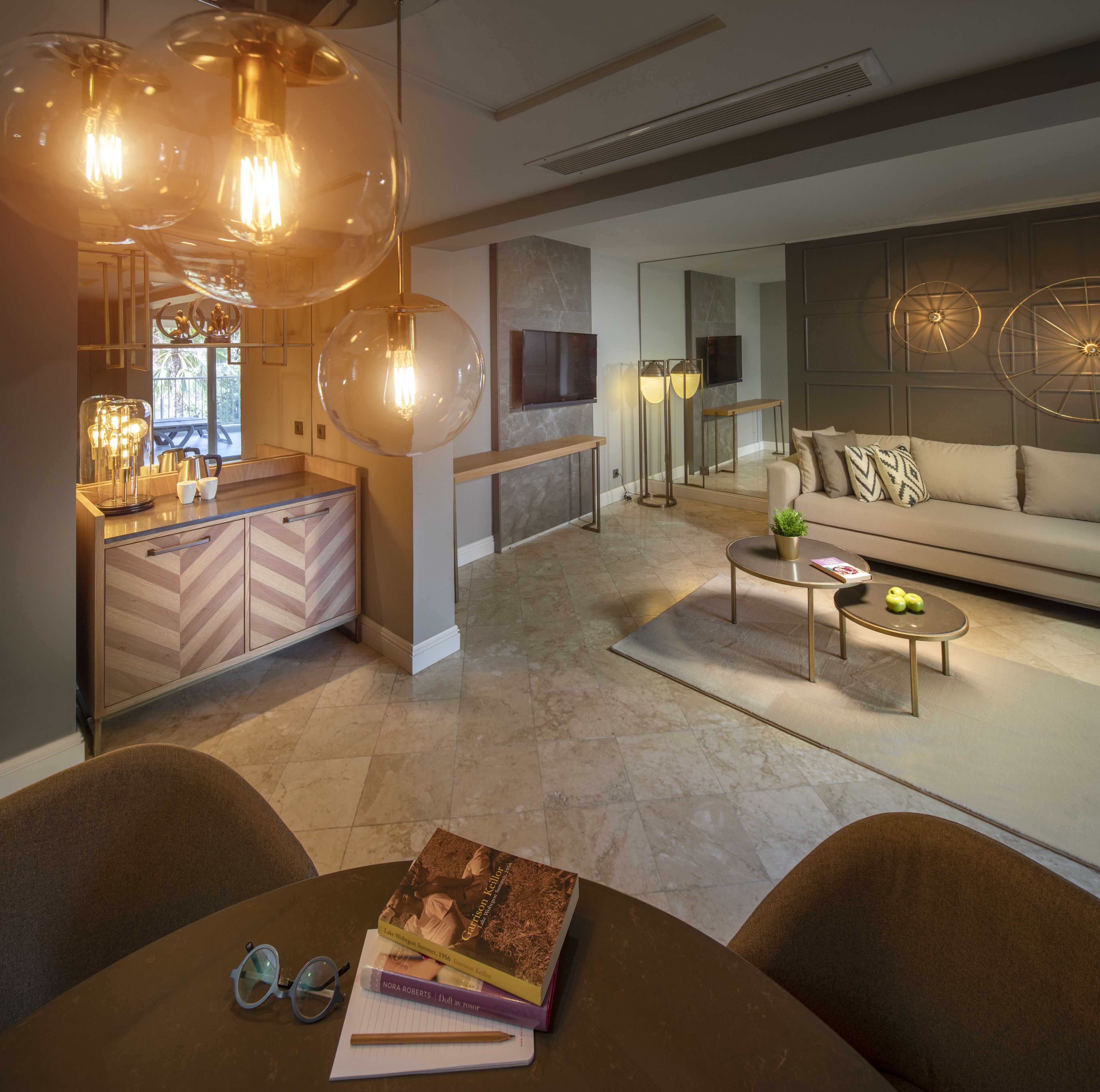 Een moderne woonkamer met een bank, salontafel en hanglampen. Er is een eethoek met een tafel en stoelen.