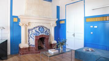 Een kamer met een open haard met blauwe en witte tegels, een witte deur en een blauwe wand met gouden sierlijsten.