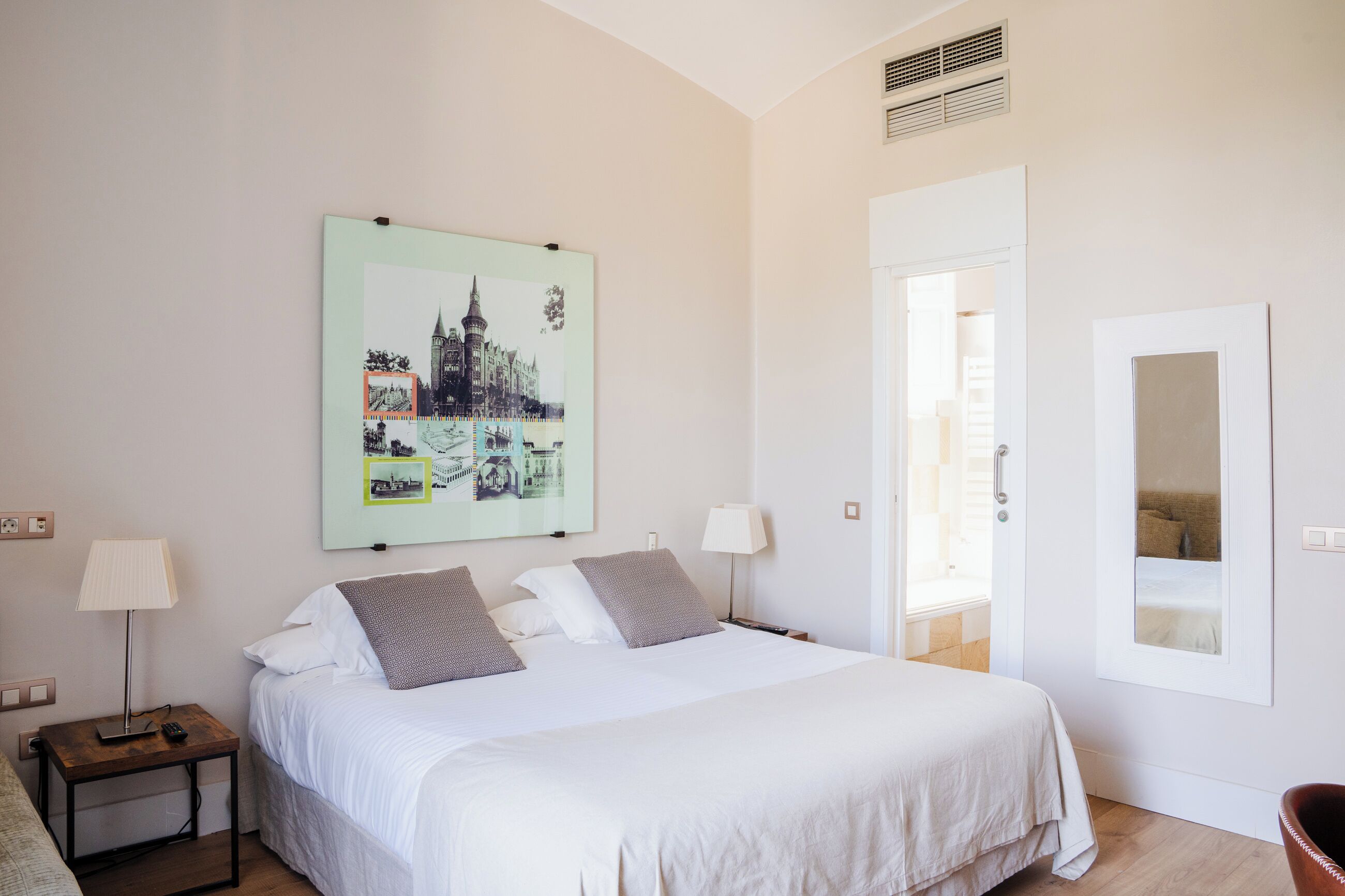 Un dormitorio con cama, dos mesitas de noche, un velador, un cuadro en la pared, una puerta y una ventana.
