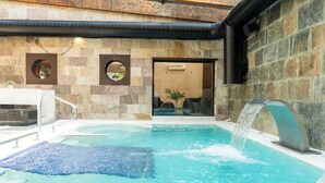 Een wellnessruimte met een jacuzzi, een klein zwembad en een stenen muur met ronde spiegels.