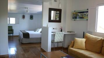 Una habitación moderna y luminosa con cama, sofá, escritorio y silla. Cuenta con ventana que proporciona luz natural y un espejo montado en la pared.