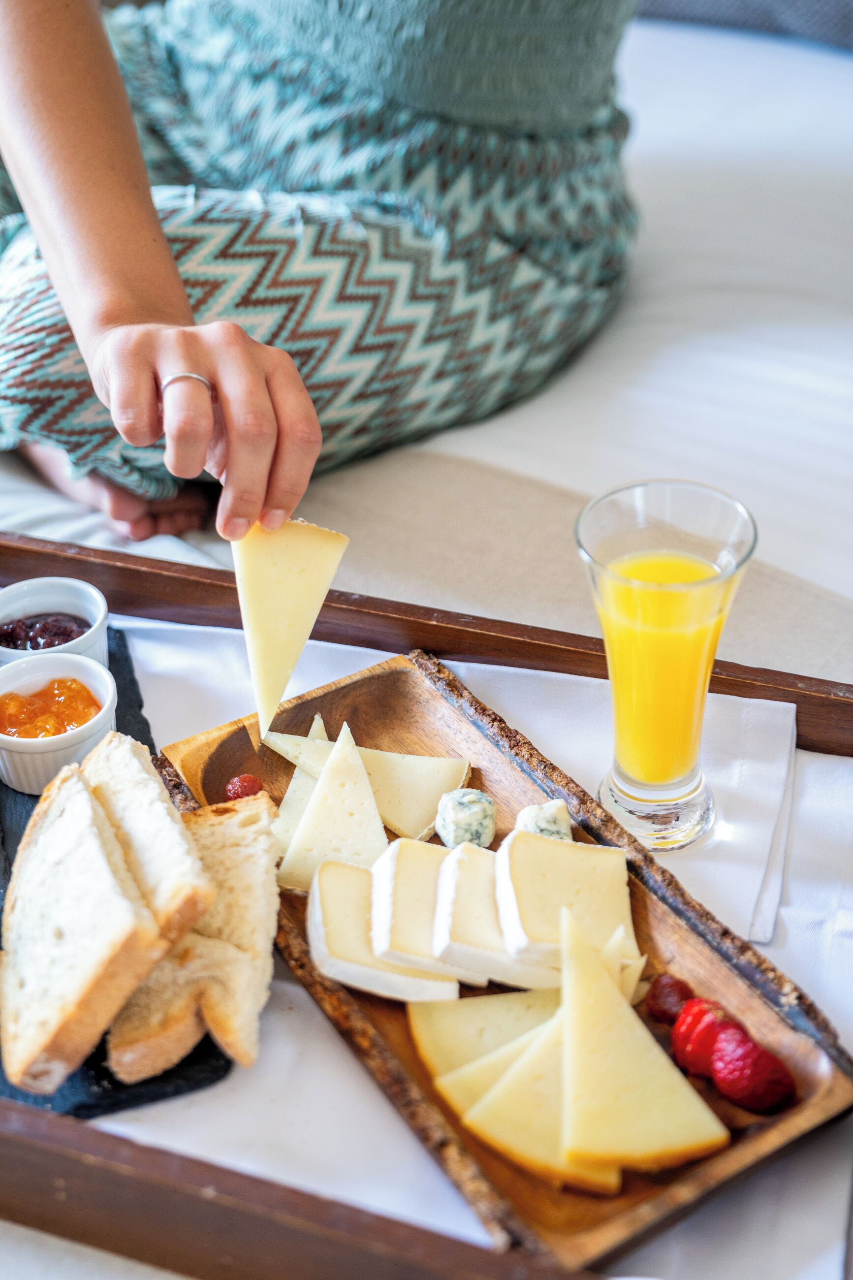Una bandeja con queso, pan y un vaso de jugo de naranja sobre una cama.