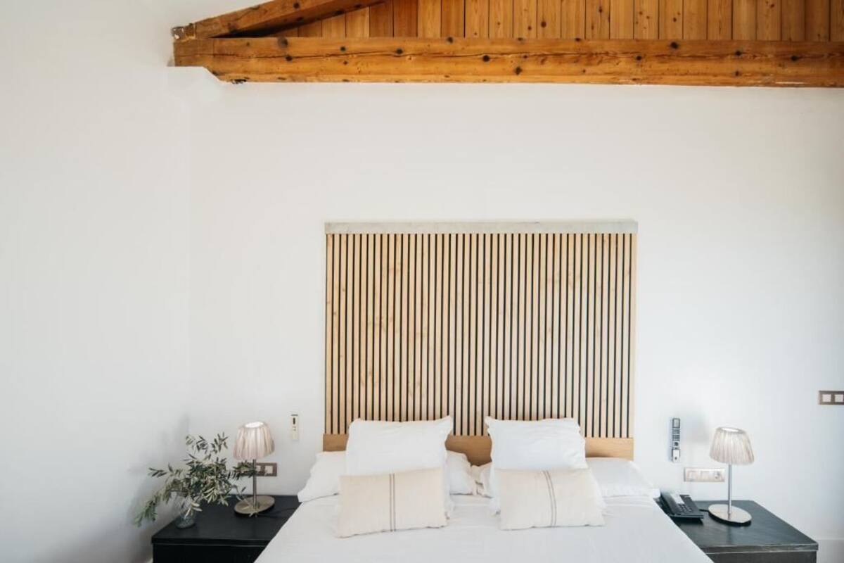 Quarto com cabeceira de ripas de madeira, cama com roupa de cama branca, duas mesas de cabeceira com luminárias e uma pequena planta em vaso.