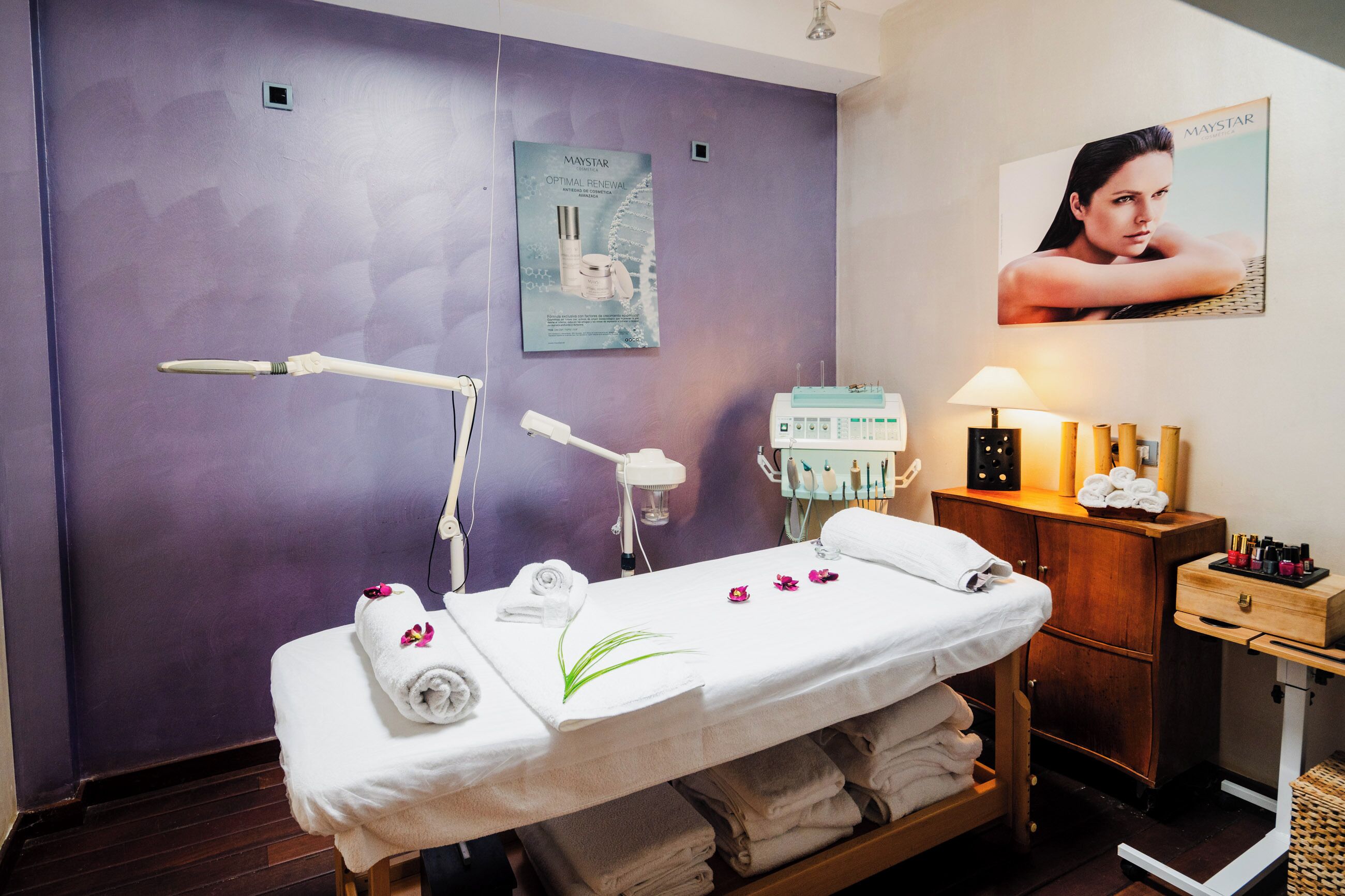 Ein Spa-Raum mit Massageliege, Handtüchern, einer Lampe und einem Poster an der Wand.