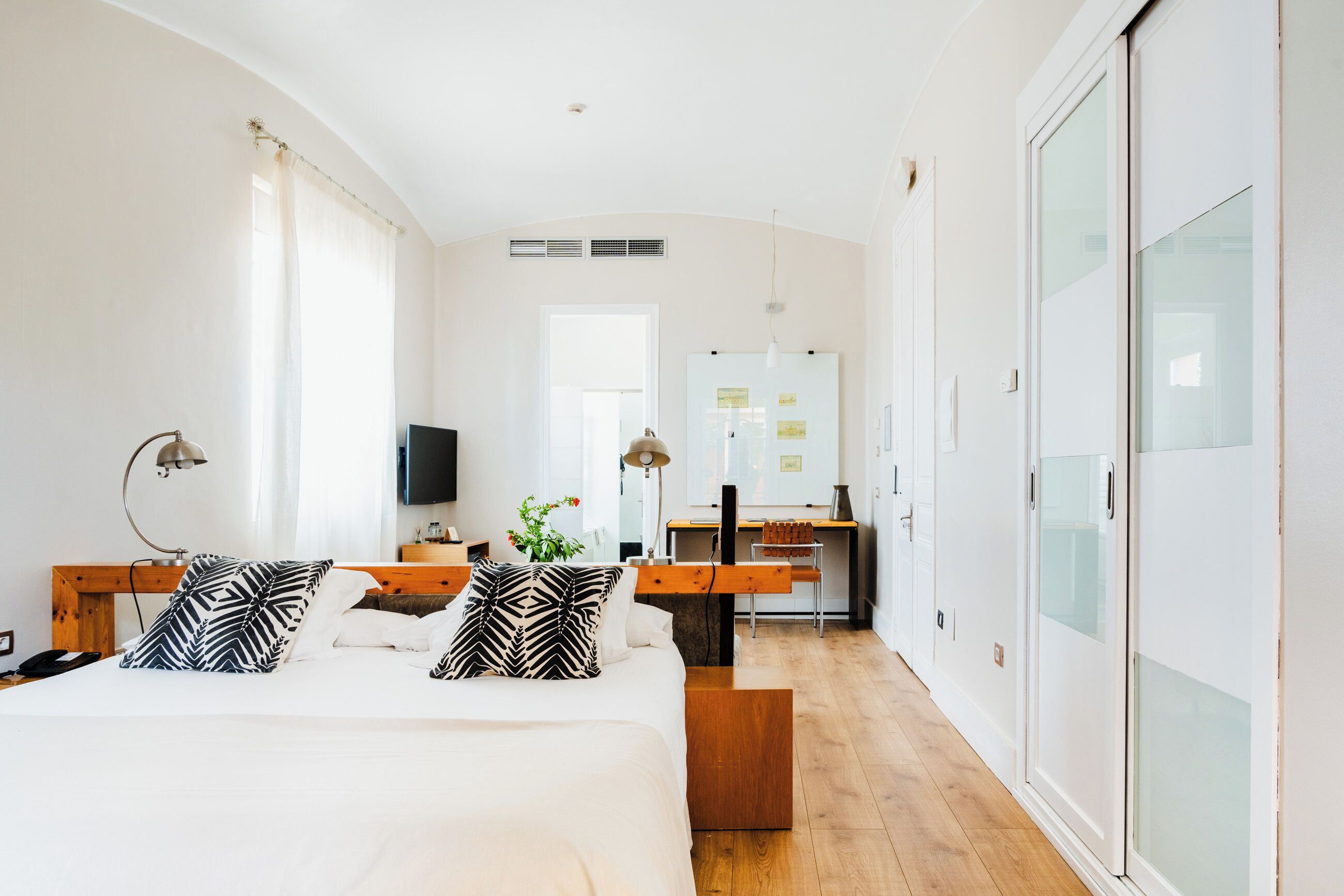 A modern hotel room with a large bed, a desk, and a wardrobe.
