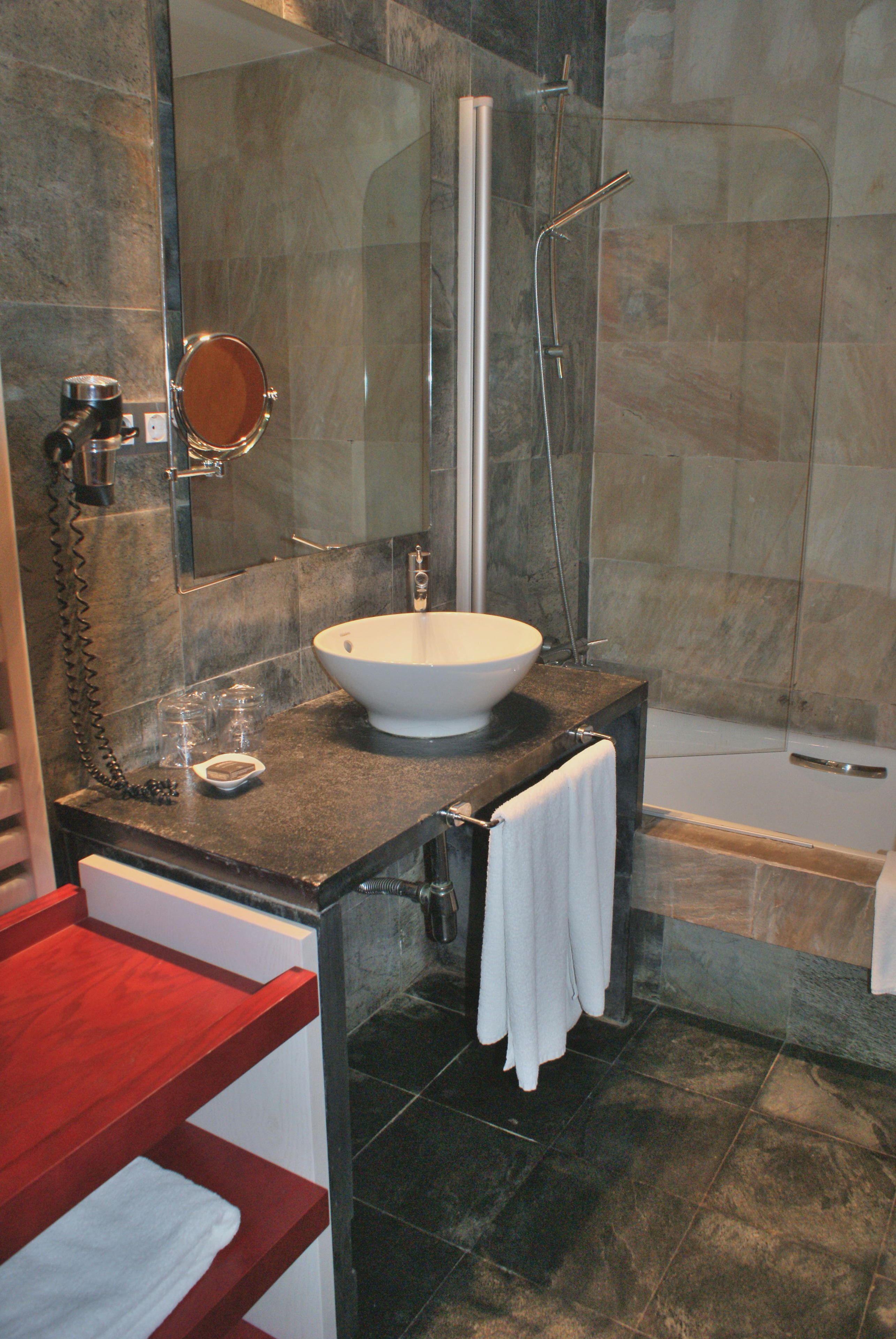 Un baño moderno con ducha envuelta en vidrio, un lavamanos blanco y un tocador rojo.