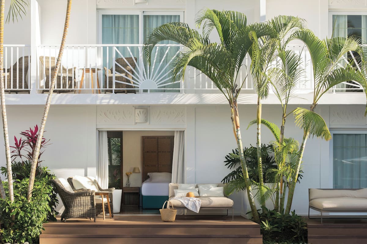Un hôtel doté d'un balcon aménagé avec des meubles en osier, un lit et des plantes en pot.