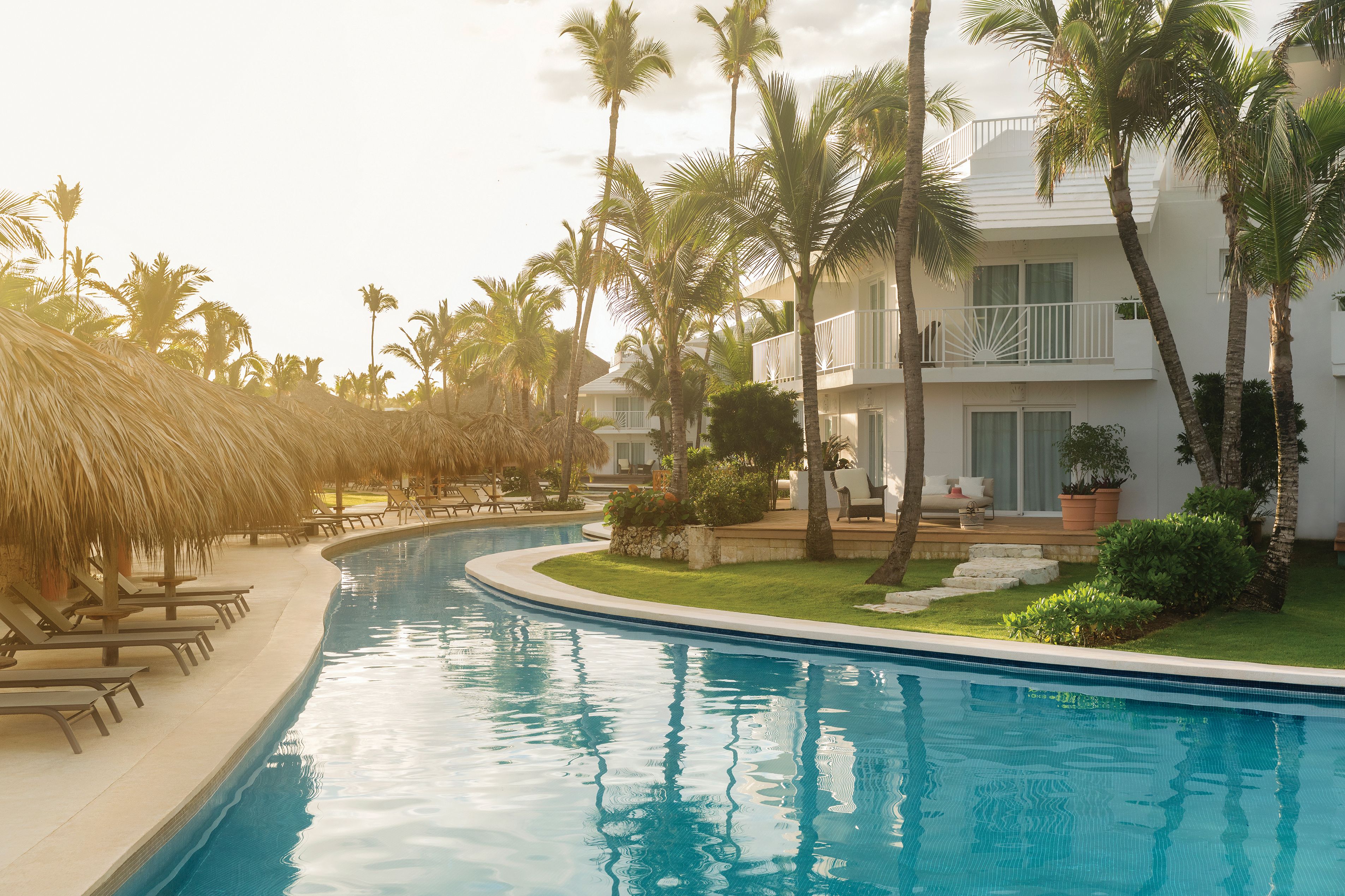 A swimming pool with lounge chairs, palm trees, and a building with balconies.