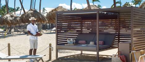 Un salón junto a la playa con estructura de madera, una mesa de billar y un sillón de playa.