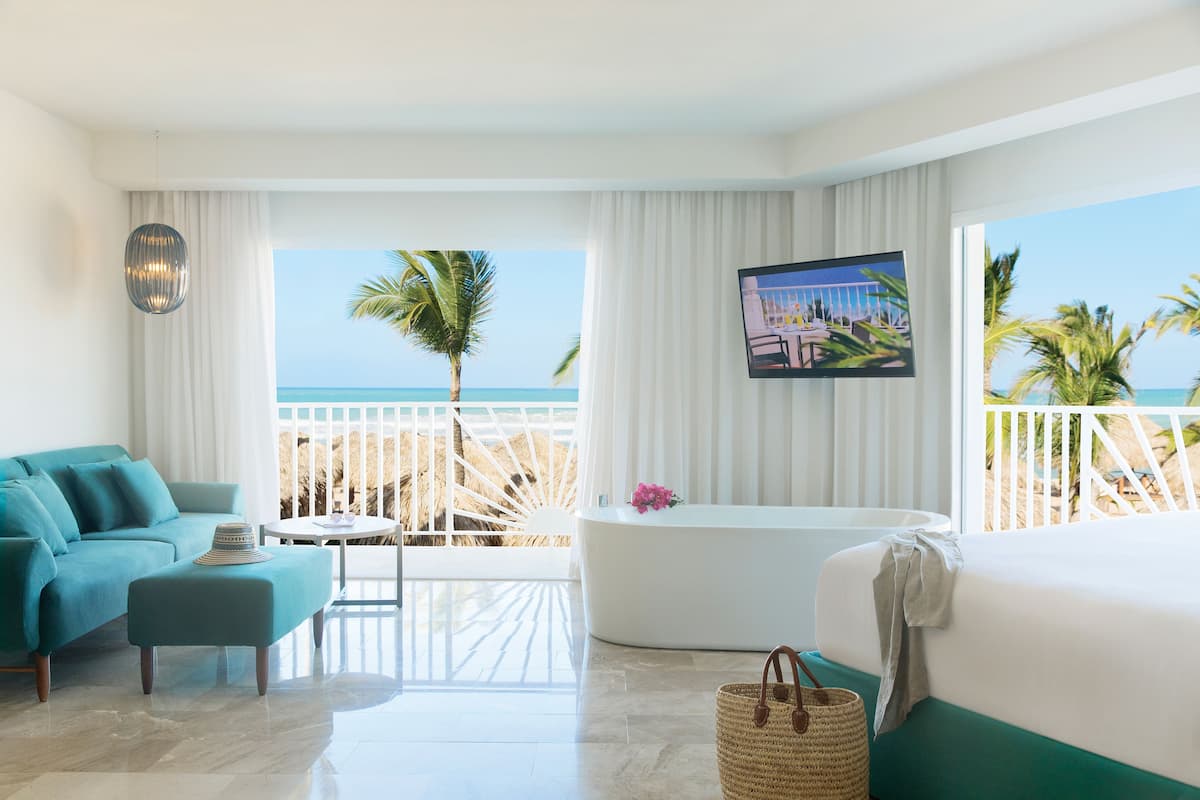 Une chambre d’hôtel moderne avec vue sur l’océan, une grande baignoire, un canapé et une table à manger.