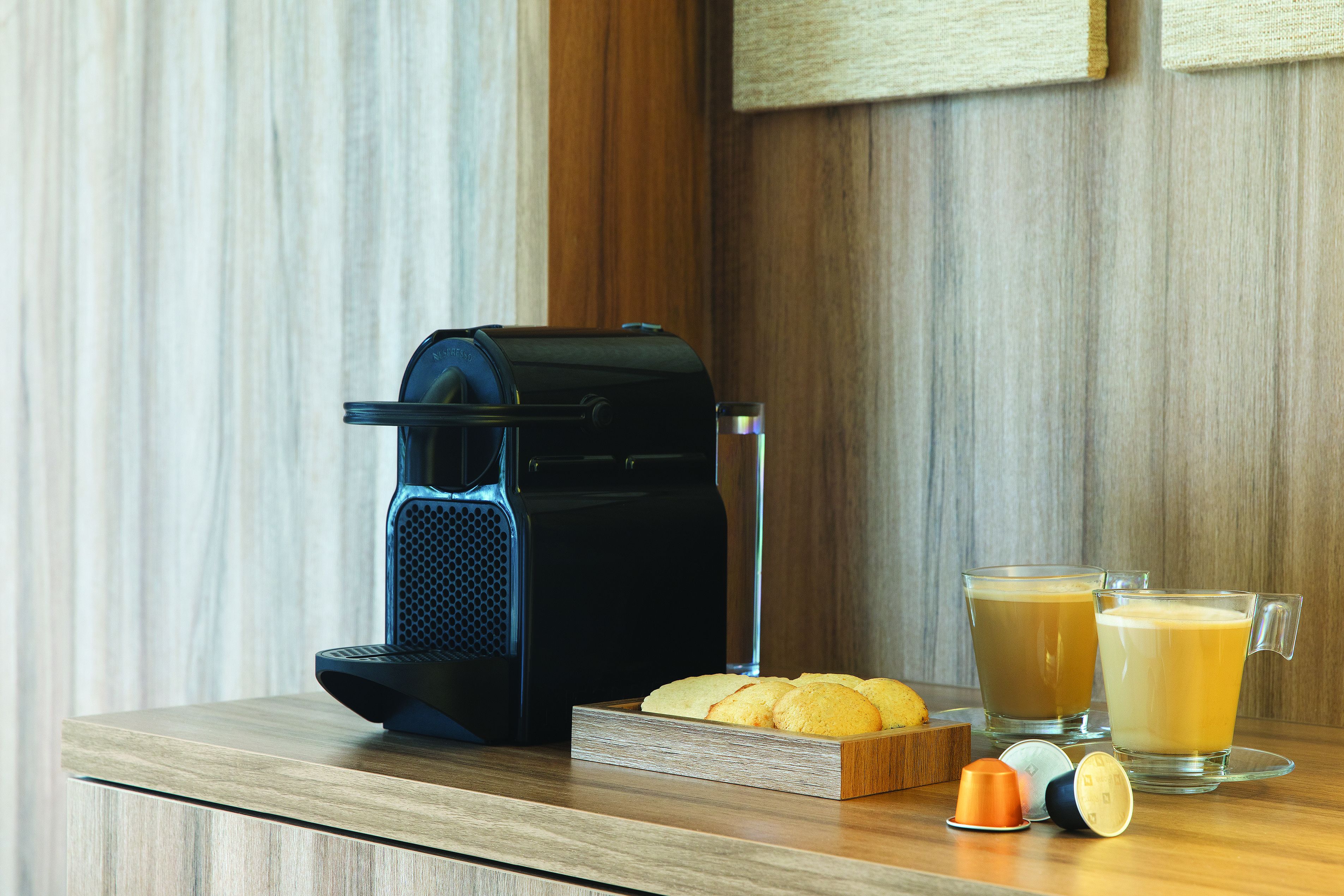 Une machine à café, deux verres de café, une assiette de biscuits et une dosette de café sur une table en bois.