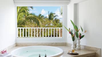 Une salle de bain avec une grande baignoire, une fenêtre donnant sur des palmiers et deux vases ornés de fleurs.