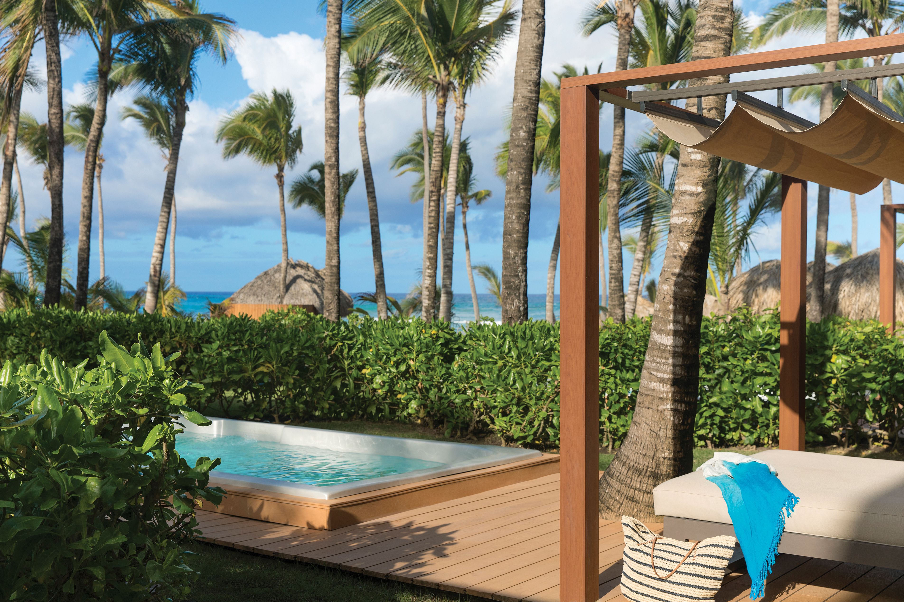 A pool area with a wooden deck, a lounge chair, and a thatched-roof structure.