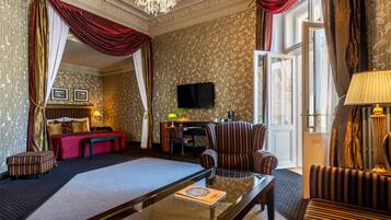 Een hotelkamer met een groot bed, een bureau met een computer, een televisie en een zithoek met een bank en fauteuils.