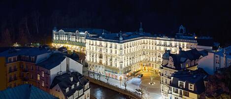 Un hotel histórico con una fachada imponente, un río al frente y un puente que lo conecta con el edificio principal.