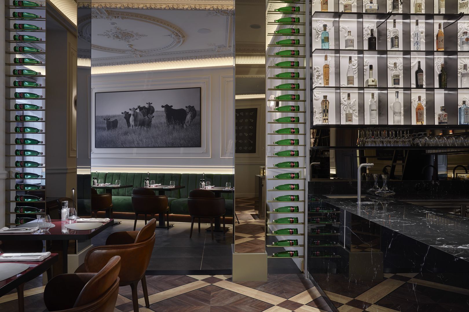 A restaurant with a bar area, green upholstered seating, and a large framed picture of cattle on the wall.