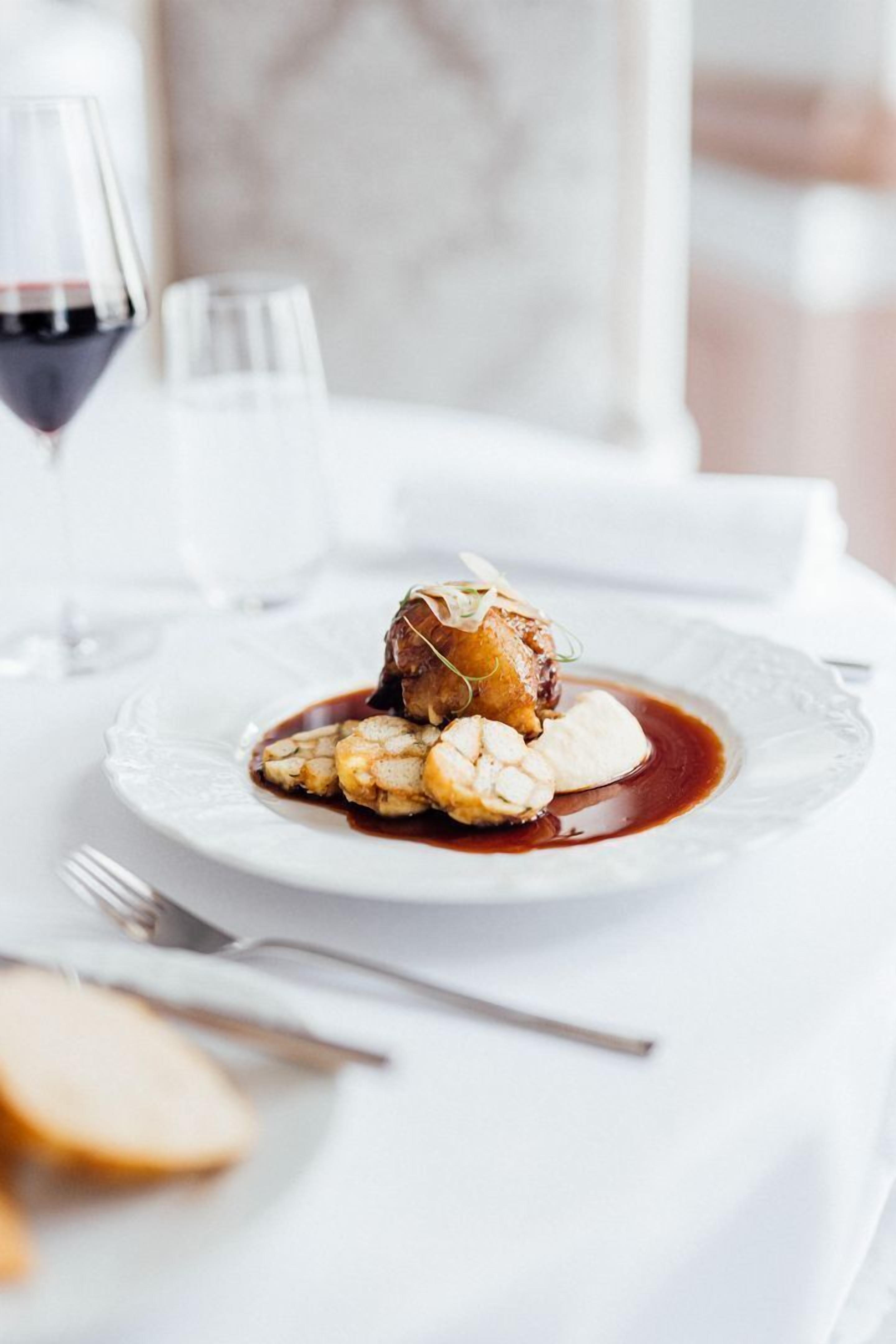 A dining table with a plate of food, a glass of red wine, and a white tablecloth.