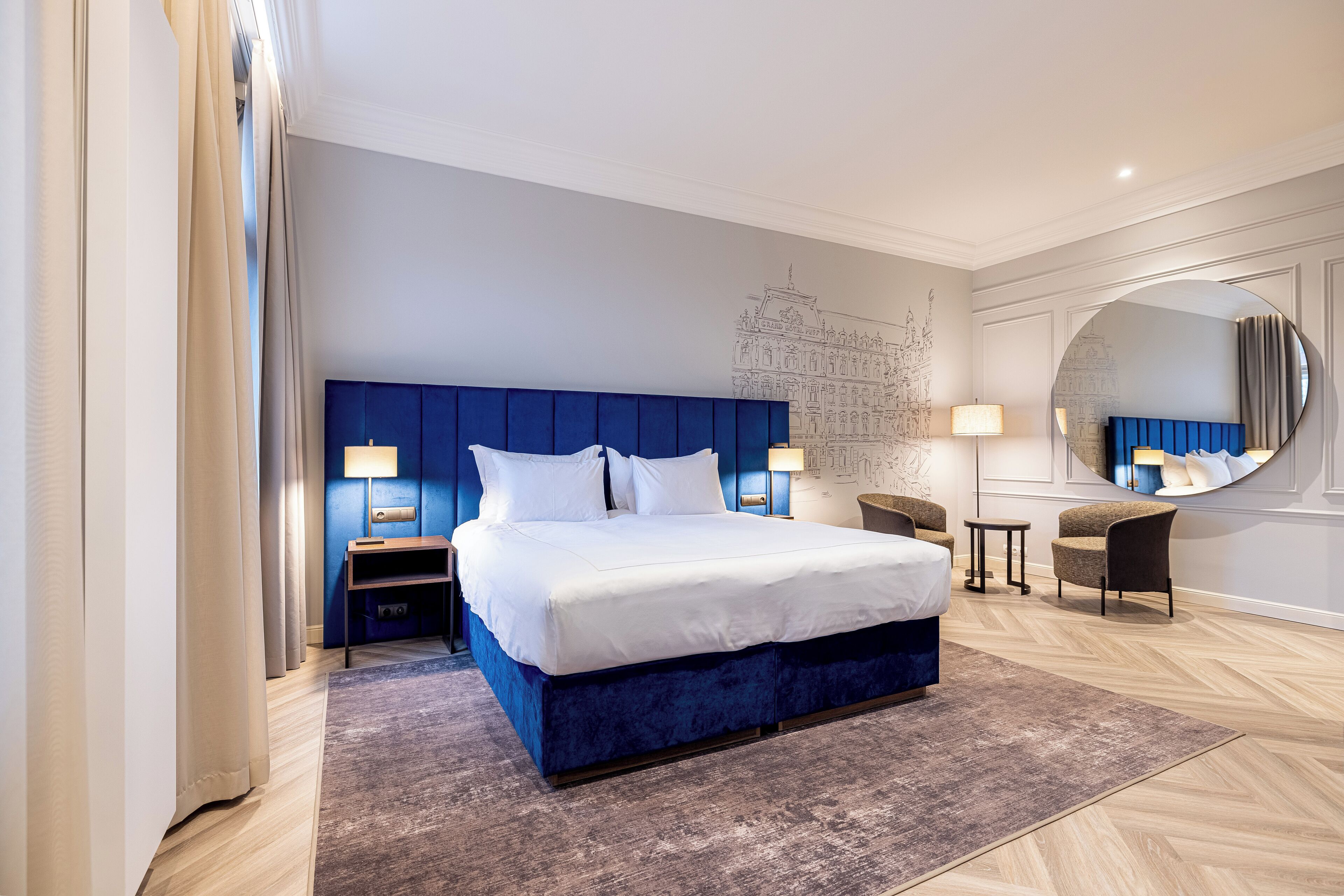 A modern hotel room with a large bed, a round mirror, a desk, and a chair.