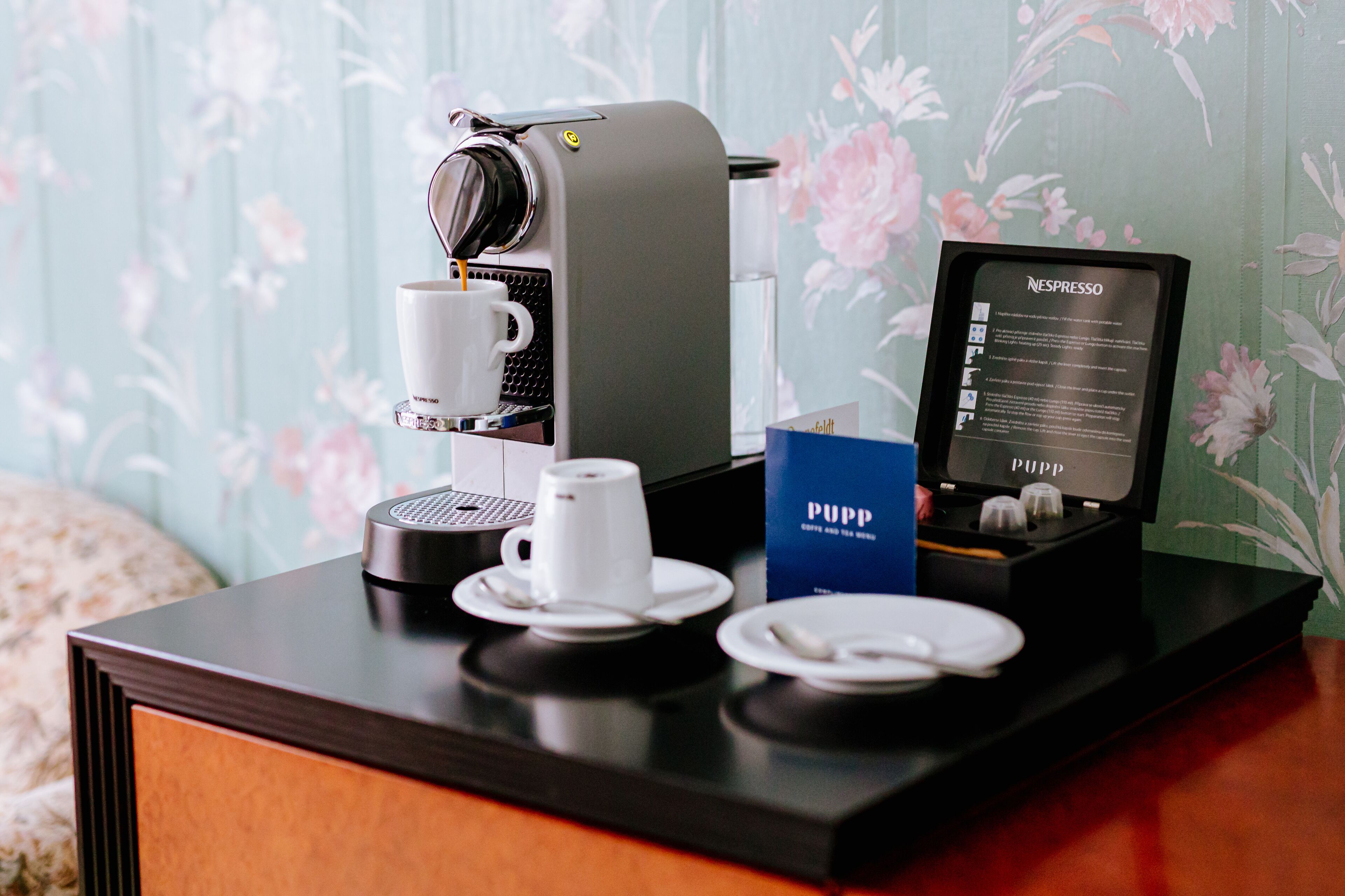 A coffee machine with a cup and saucer, a PUPP coffee pod box, and a Nespresso coffee pod box on a wooden table.