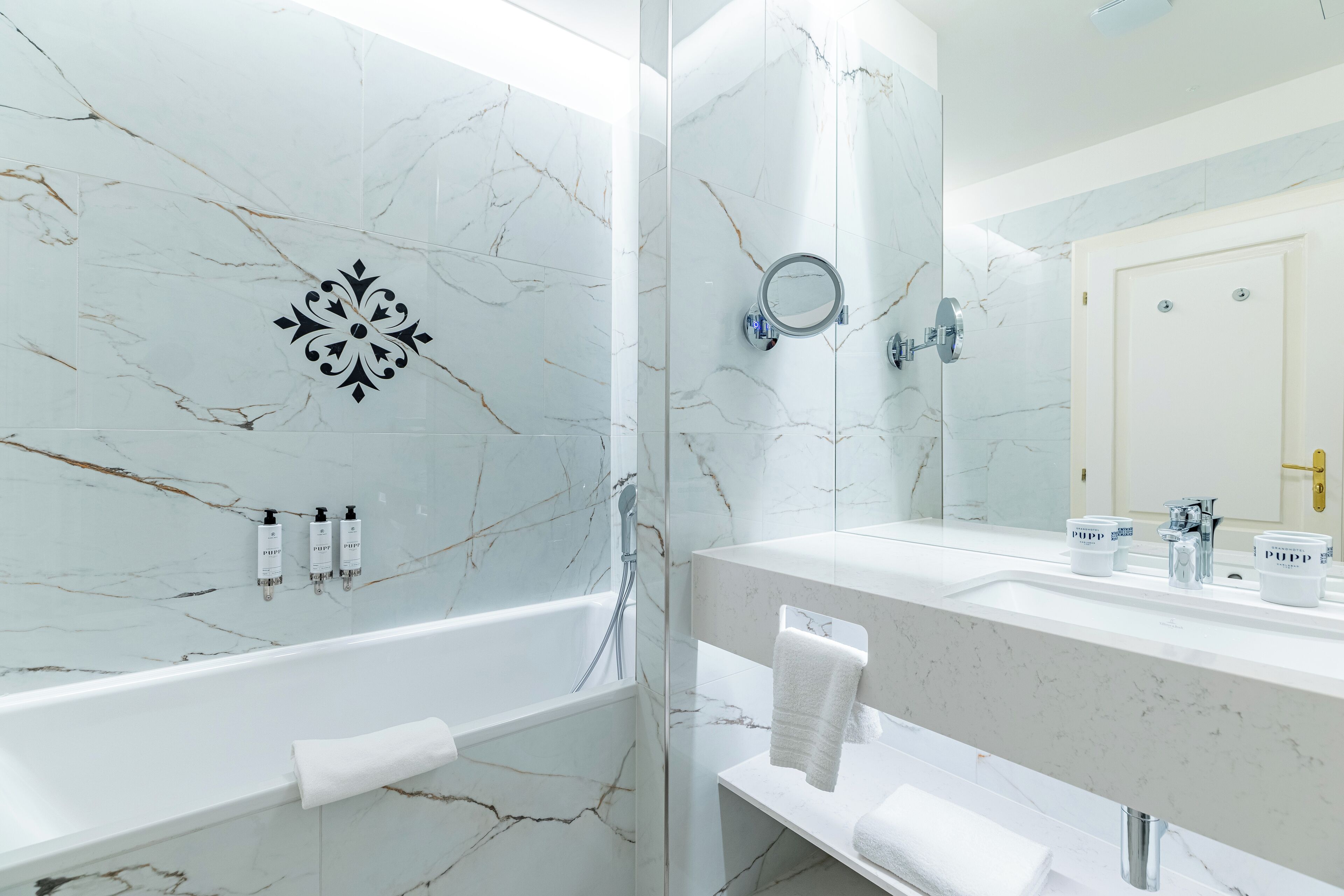 A modern bathroom with a marble wall, a bathtub, a sink with a mirror, and toiletries.