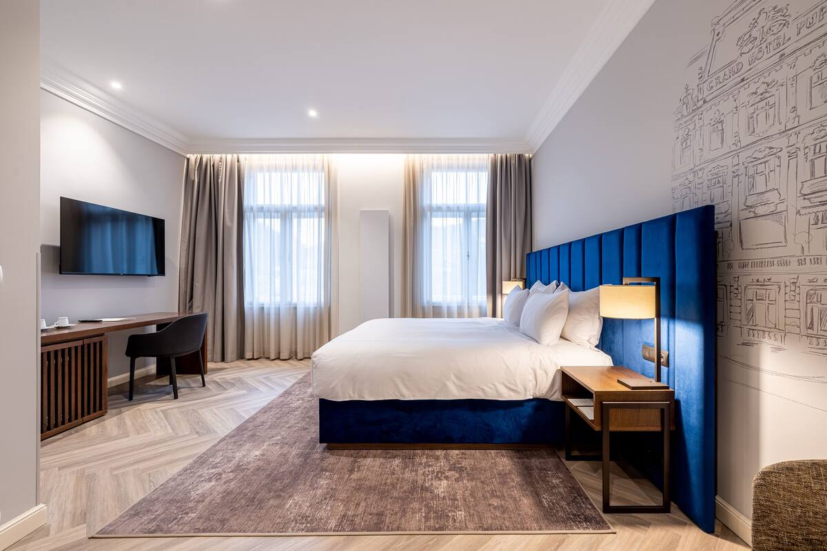Quarto de hotel moderno com uma cama grande, uma escrivaninha, televisão e uma parede de destaque azul.