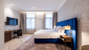 Una camera d'hotel moderna con un letto grande, una scrivania, un televisore e una parete azzurra.