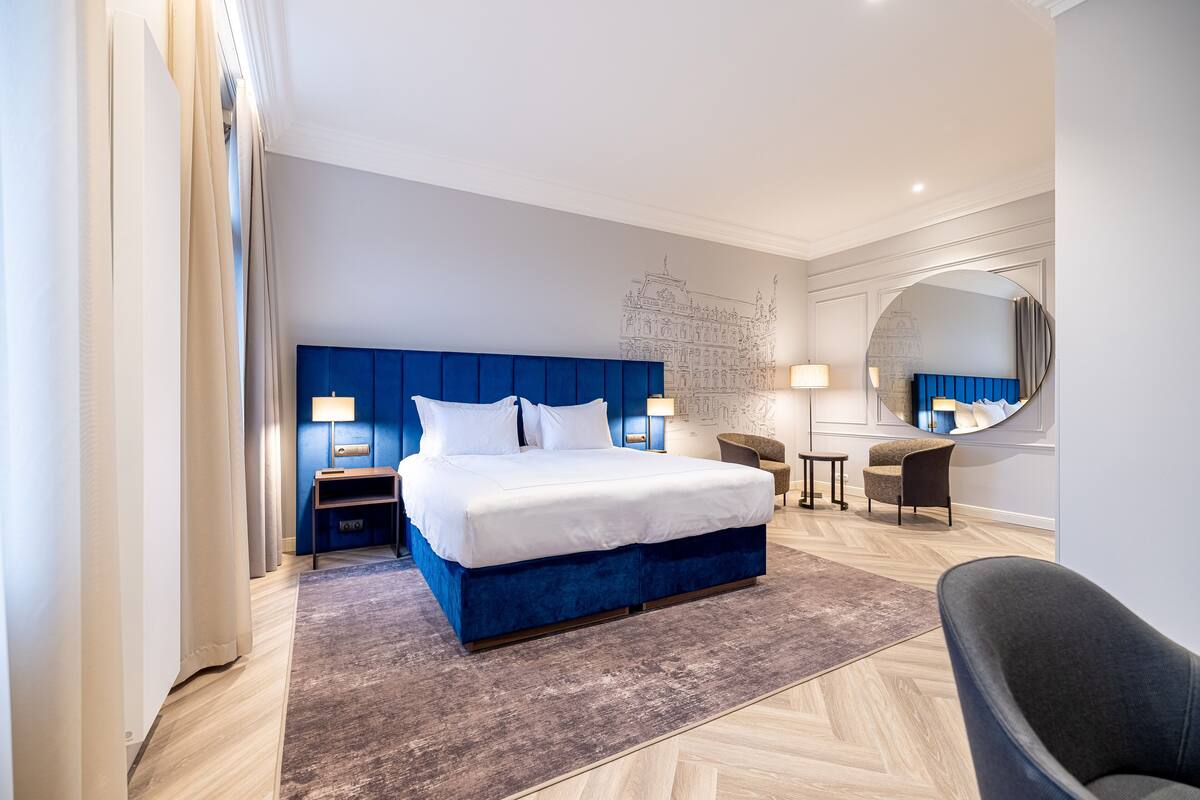 Quarto de hotel moderno com uma cama grande, uma escrivaninha, uma cadeira e um espelho.