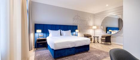 A modern hotel room with a large bed, a desk, a chair, and a mirror.