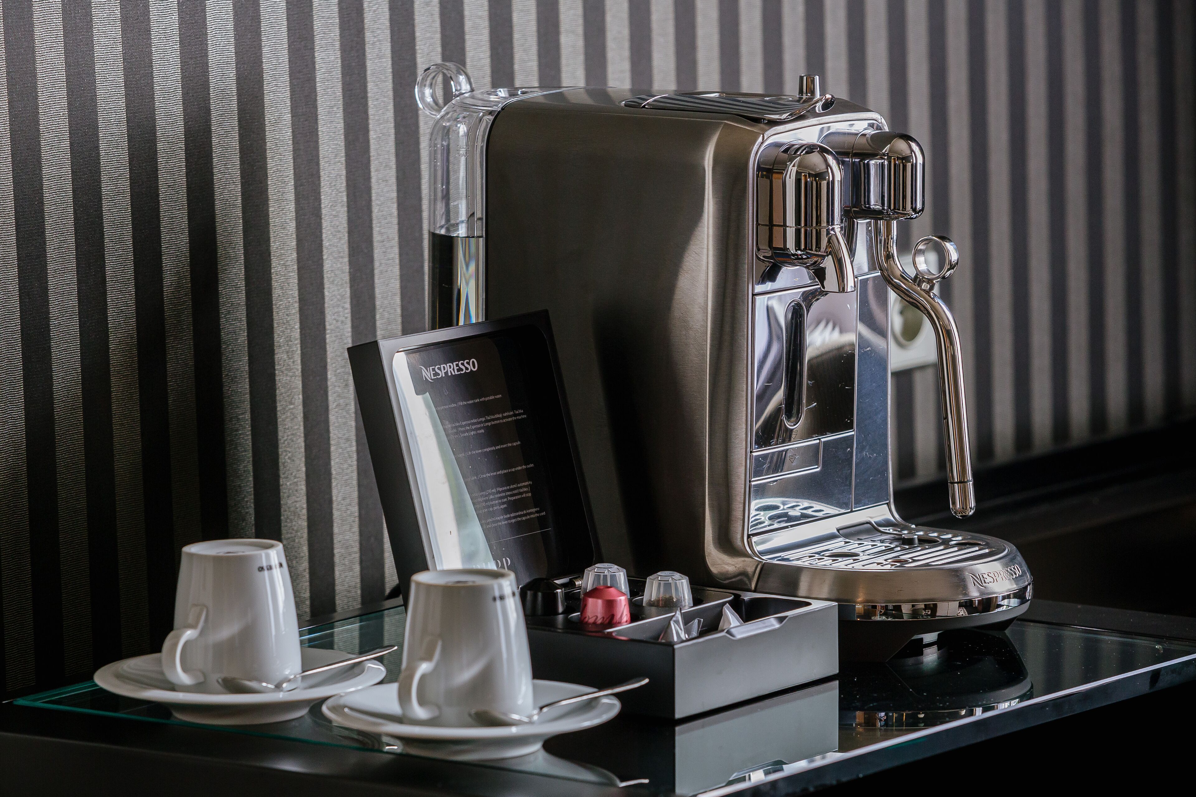 Una máquina de café Nespresso sobre una mesa de vidrio, con dos tazas blancas y un menú.