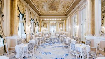 Une salle à manger luxueuse, ornée de colonnes richement décorées, de lustres et d’un sol à motifs.