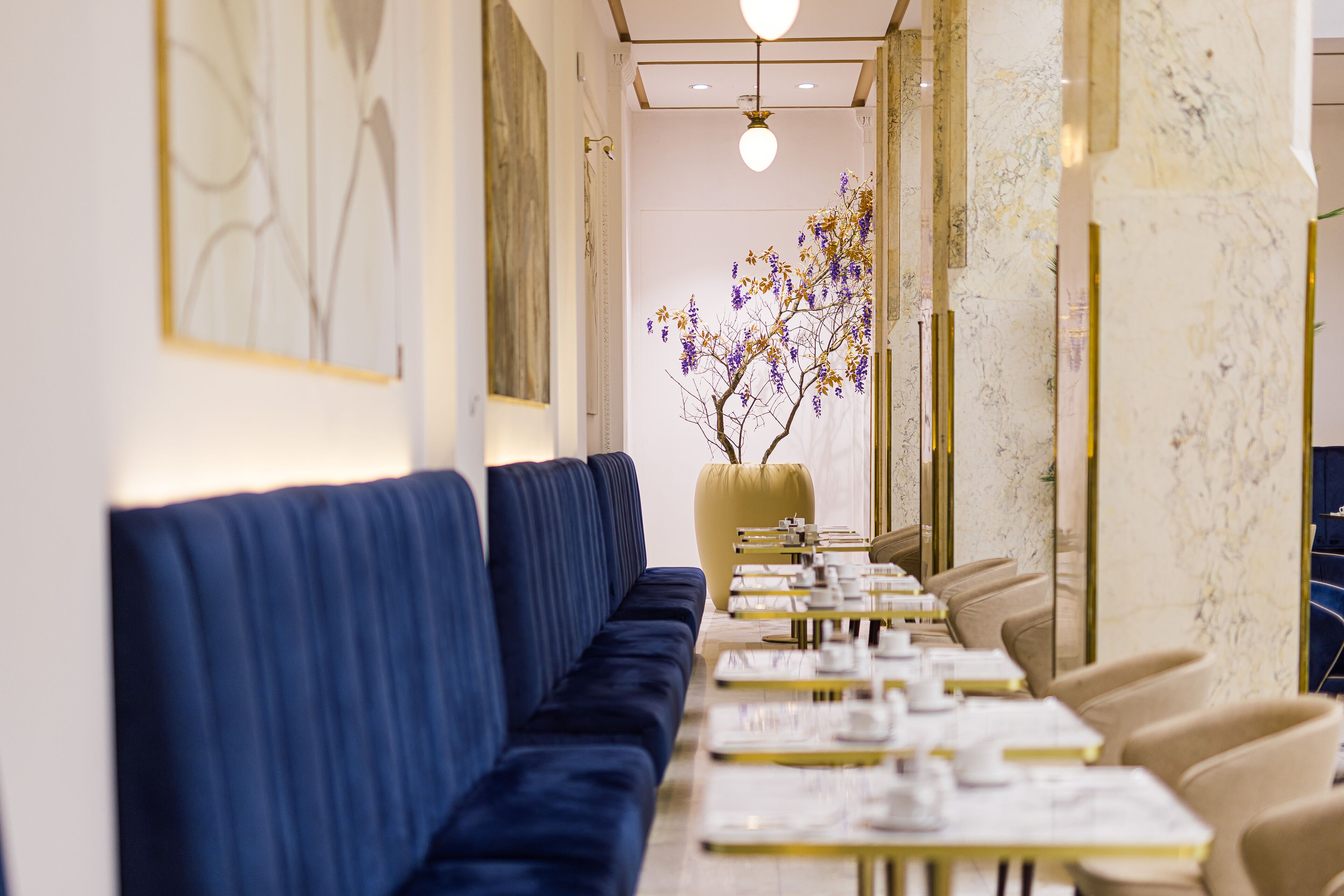 A long, narrow dining area with blue upholstered seating and tables set with white tablecloths and gold accents.