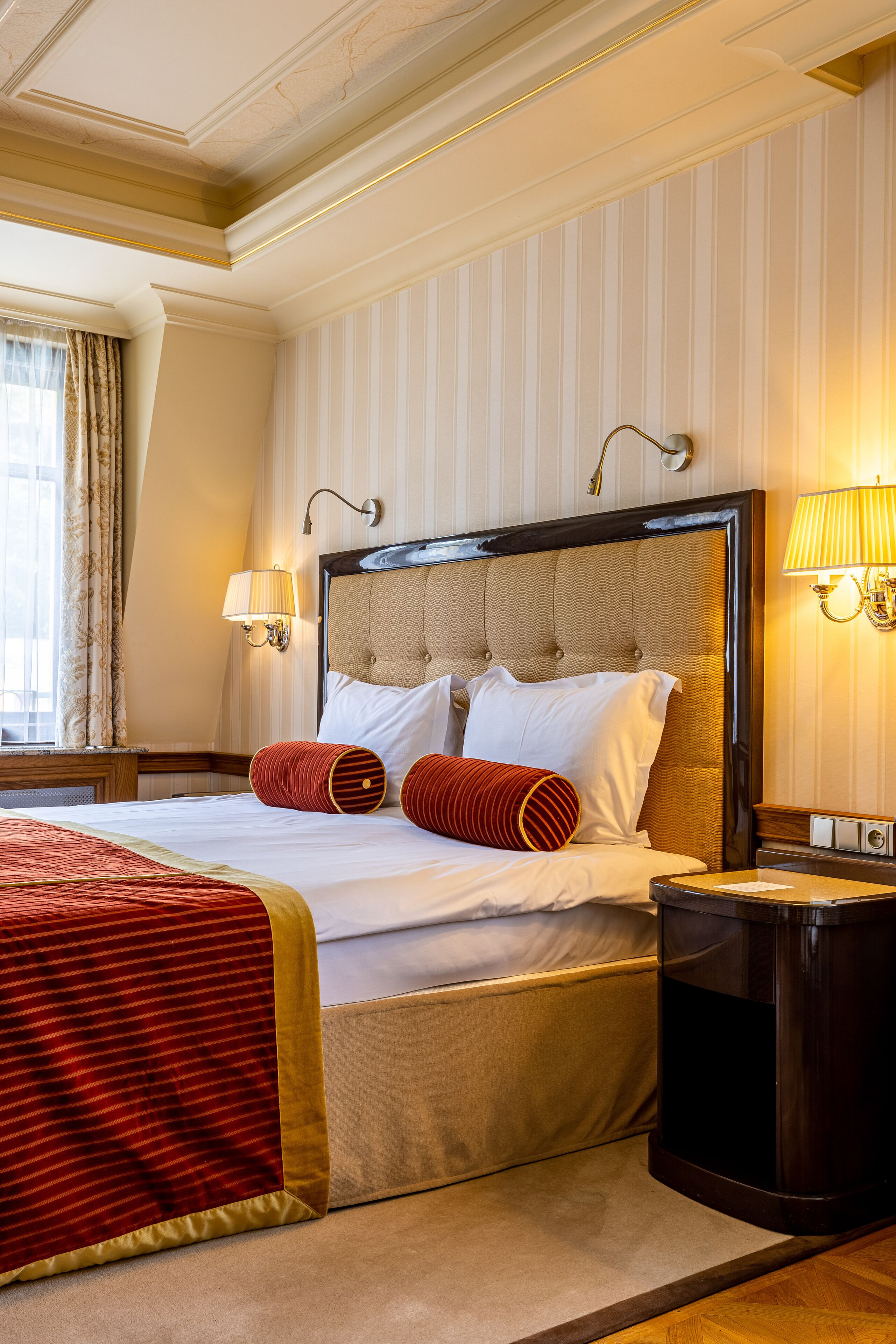 A hotel room with a large bed, striped wallpaper, and two wall-mounted lamps.