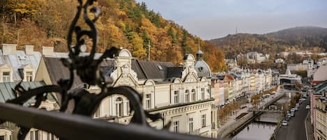 Vista de un paisaje urbano con edificios históricos, un río y una colina cubierta de follaje otoñal.