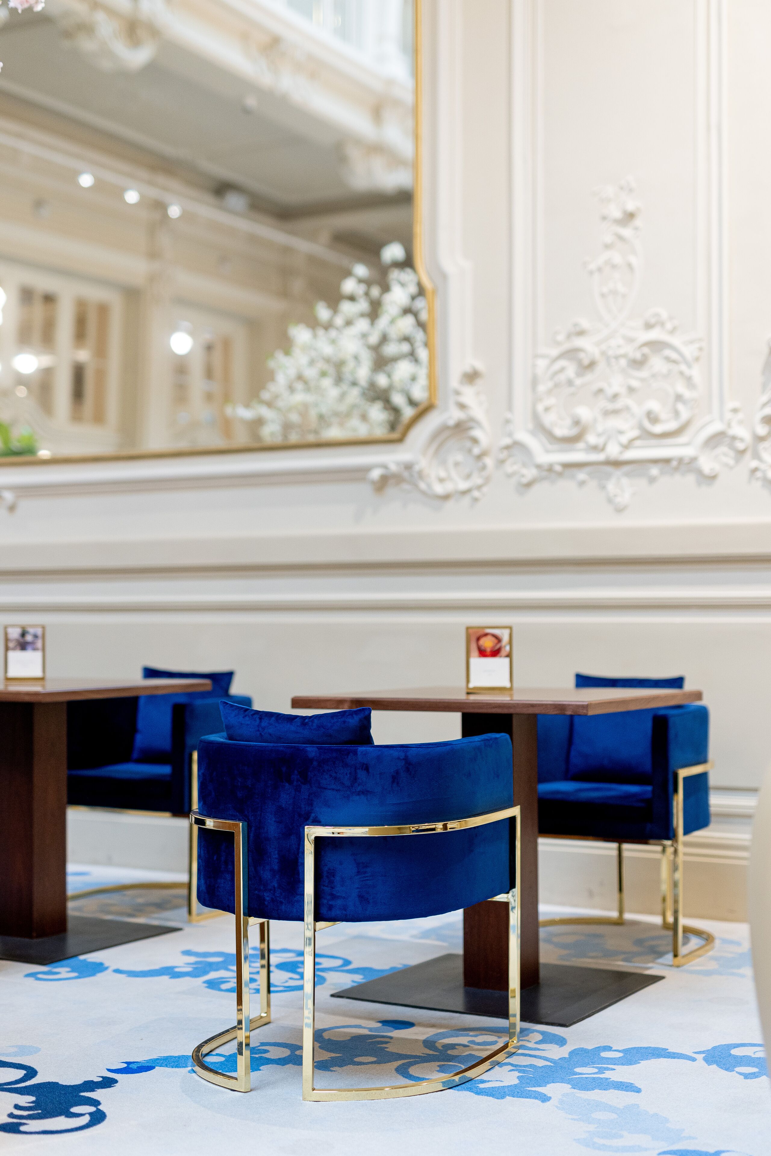A hotel lobby with blue velvet chairs, a large mirror, and ornate wall decorations.