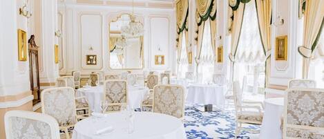 A formal dining room with ornate ceiling, chandeliers, and patterned carpet.