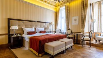 Ein geräumiges Hotelzimmer mit einem großen Bett, einer Sitzecke mit Tisch und Stühlen sowie einem Blick auf die Stadt durch große Fenster.