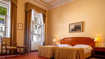 A hotel room with two beds, a chair, a table, and a window with curtains.