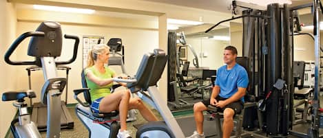 A gym with stationary bikes, weight machines, and a mirror.
