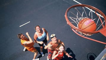 A basketball hoop on a court with a net, a basketball, and people playing.