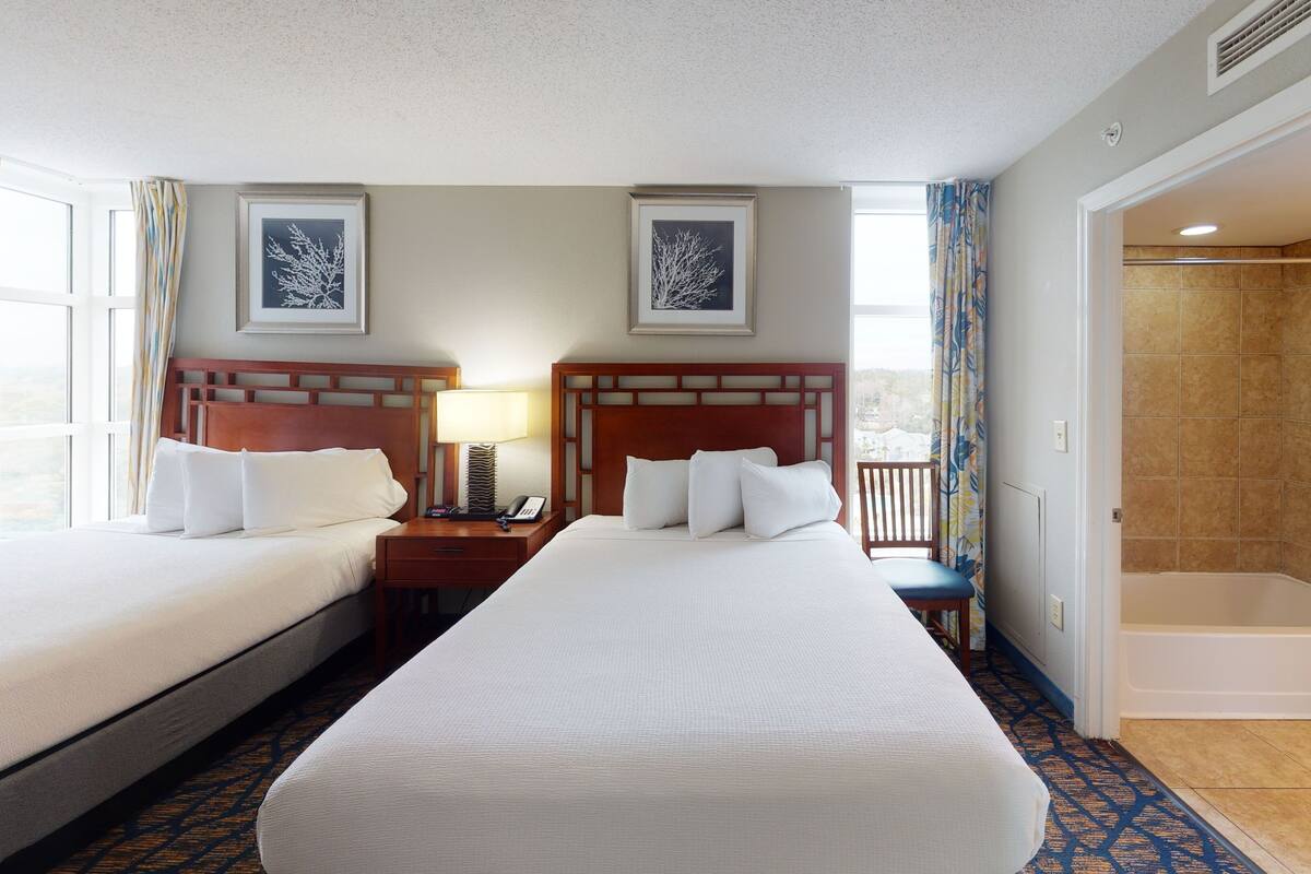 A hotel room with two beds, a nightstand with a lamp, a phone, and framed artwork on the wall.